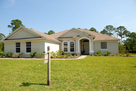 Beautiful suburban house with lush lawn, showcasing a for sale sign under a clear blue sky.